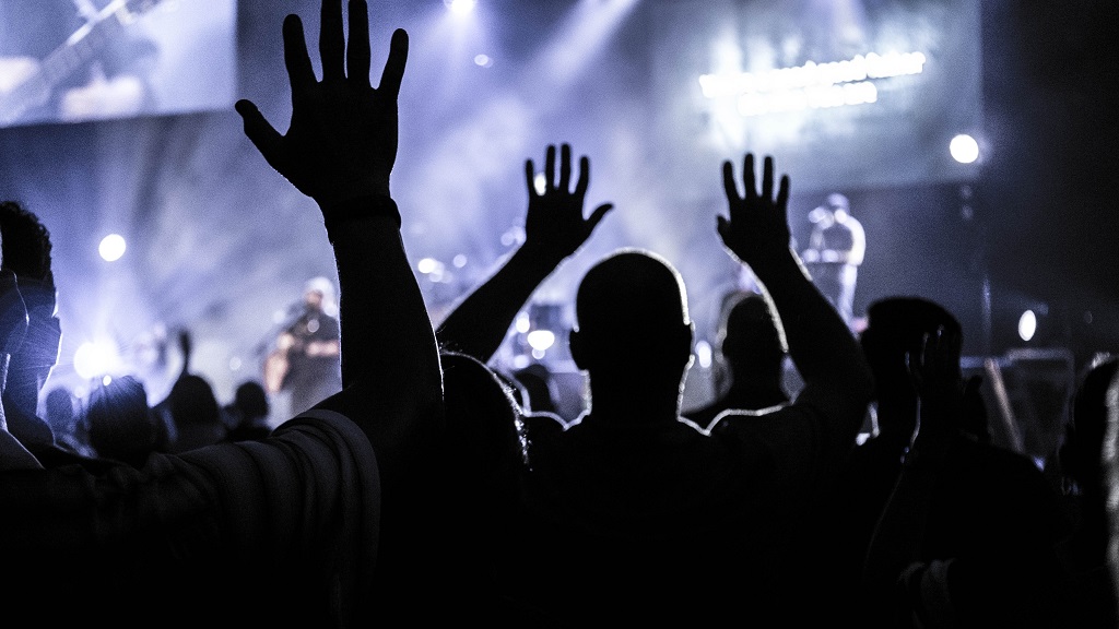 Live event crowd with hands raised, stage lighting behind